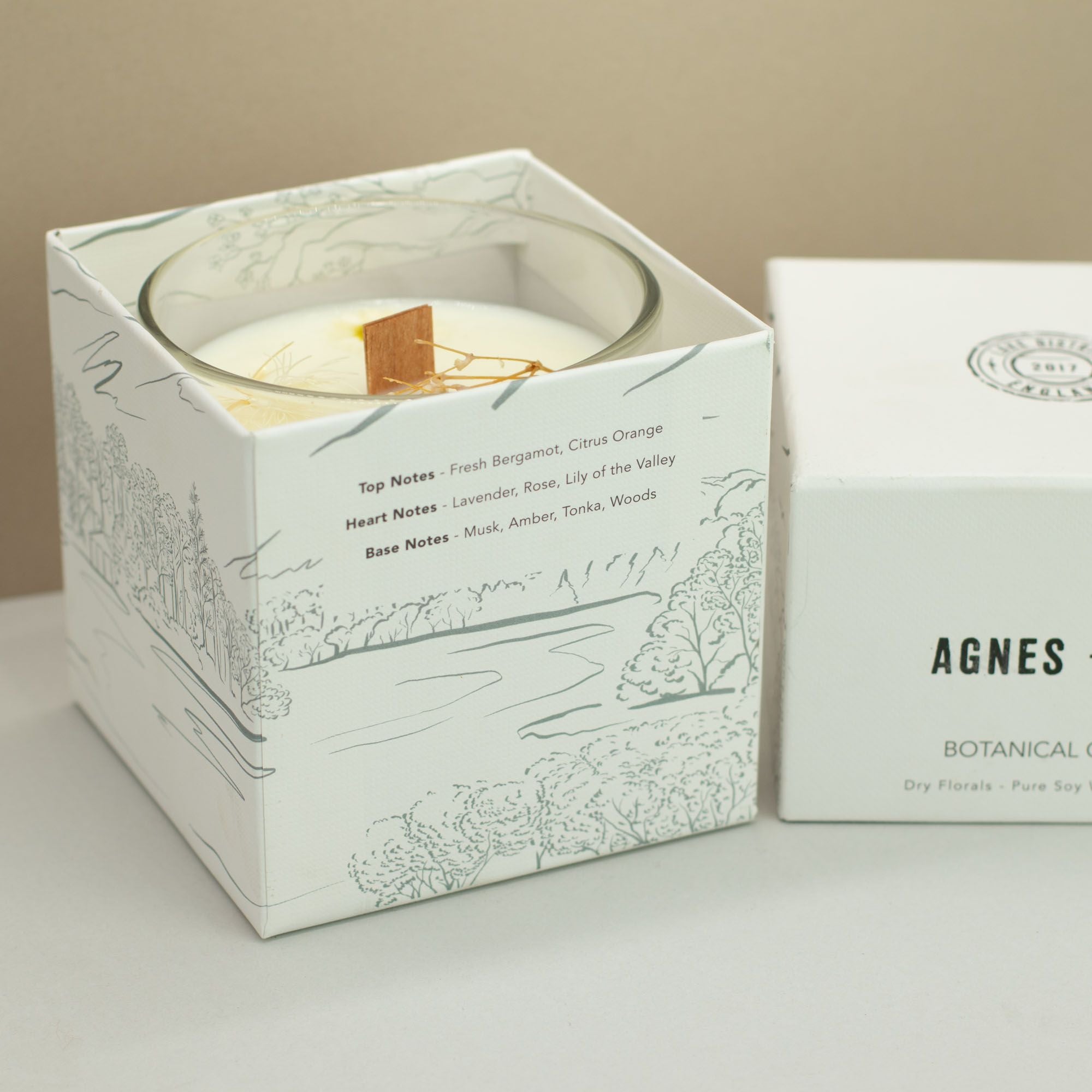 Candle in a decorative box with 'AGNES' branding on a neutral background